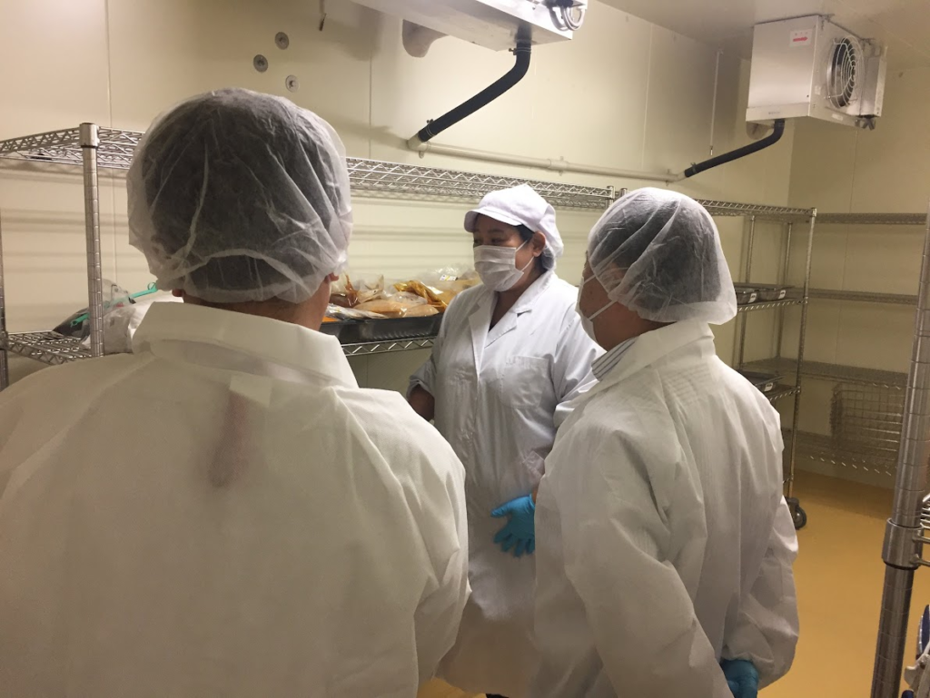 衛生管理が行き届いた厨房の保管庫前で白衣を着用したスタッフが衛生管理スキームの確認をしている様子