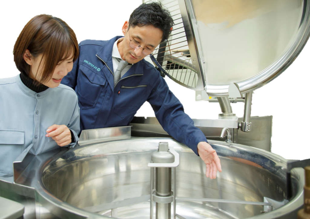 作業着の技術者が服部工業の電気式攪拌機付き回転釜ヴェスタの構造や最適な活用方法を説明している様子